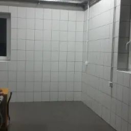 Wnętrze po remoncie: białe płytki na ścianach, szara podłoga. Widoczne okna i żółty nagrzewnica. Nowoczesny minimalizm, czyste linie, świeżo wykończone pomieszczenie.