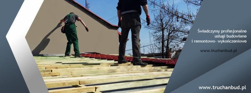 Dwóch pracowników na dachu z drewnianą konstrukcją i czerwonymi płytami. Jeden w zielonym kombinezonie, drugi w czarnych spodniach. W tle budynek.