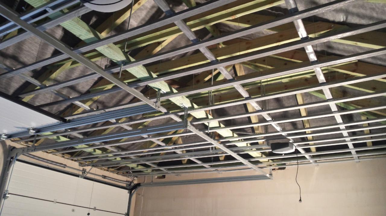 Stelaż sufitowy z profili metalowych, widoczne drewniane elementy konstrukcyjne dachu. W tle brama garażowa z automatycznym napędem.