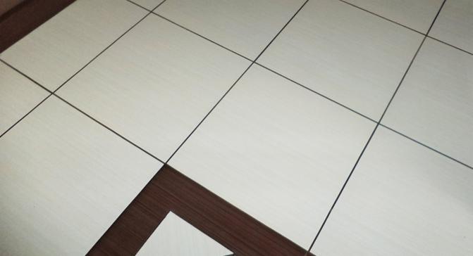 Jasne, kwadratowe płytki podłogowe z ciemnymi fugami i dekoracyjnym, geometrycznym wzorem z ciemnego drewna w rogu. Minimalistyczny design podłogi.