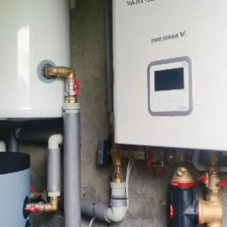 Instalacja kotła grzewczego z zbiornikiem buforowym i filtrem, rury izolowane, logo firmy Topinstall na urządzeniu.