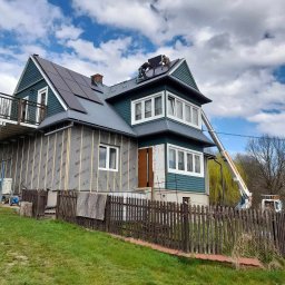 Topinstall - Montaż paneli fotowoltaicznych na dachu dwupiętrowego domu z podnośnika koszowego; widoczne ocieplenie ścian zewnętrznych budynku.