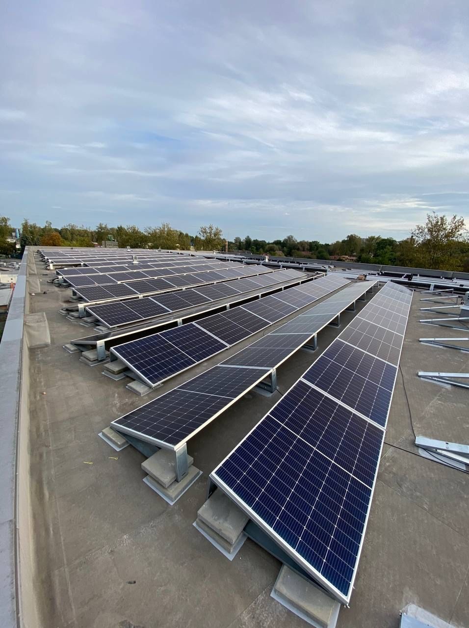 Widok z góry na rzędy paneli słonecznych zamontowanych na płaskim dachu z widocznymi elementami konstrukcyjnymi i fragmentami niezamontowanych profili aluminiowych.