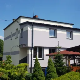 Dwukondygnacyjny dom z szarą i białą elewacją w poziome pasy, widok z ogrodu z iglakami.