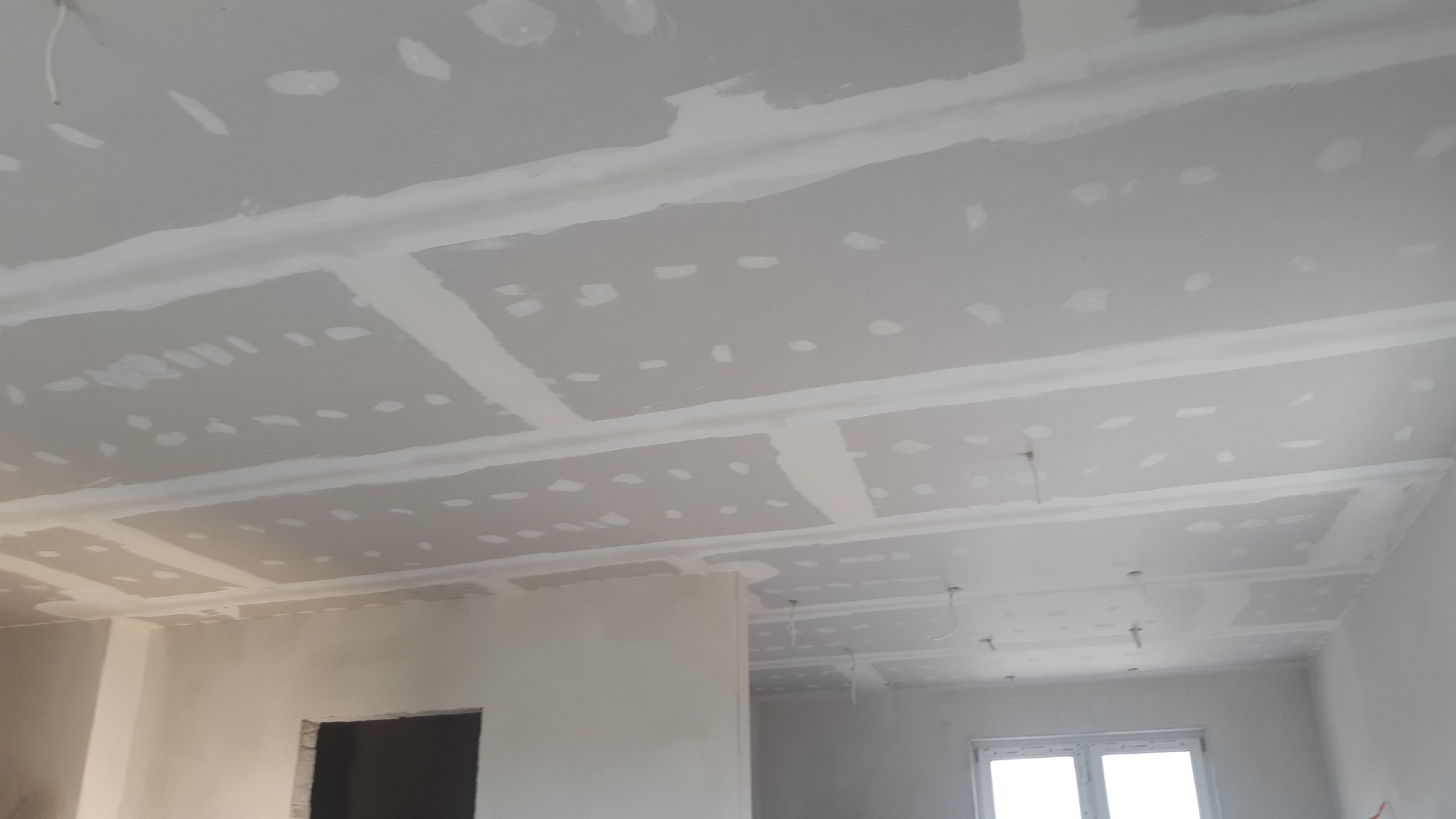 Sufit z płyt gipsowo-kartonowych po szpachlowaniu łączeń, widoczne niedoskonałości i miejsca wymagające dodatkowego szlifowania, surowy stan wnętrza.