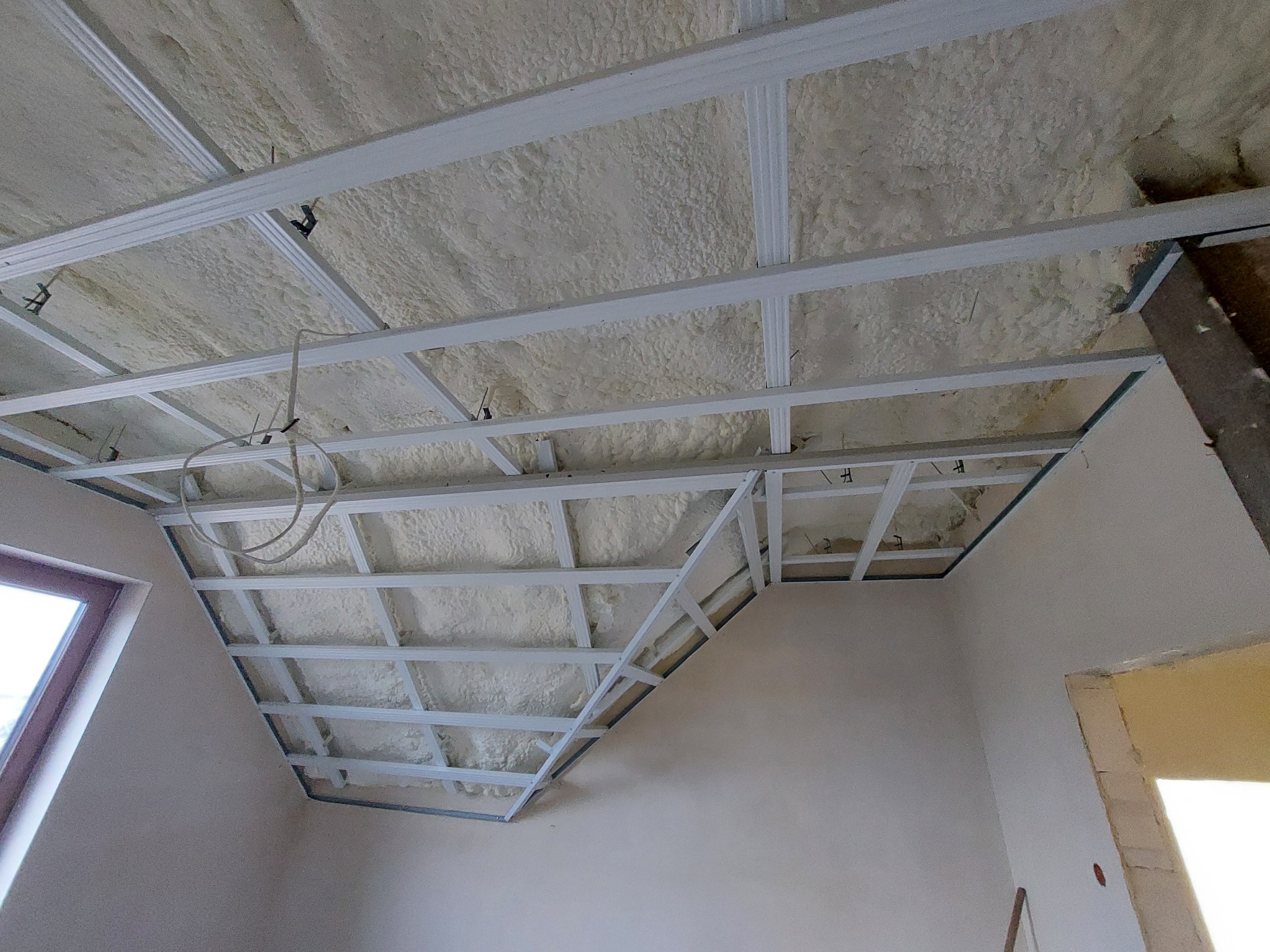 Sufit poddasza z widoczną izolacją natryskową z pianki poliuretanowej i metalową konstrukcją pod płyty gipsowo-kartonowe, widoczne kable elektryczne