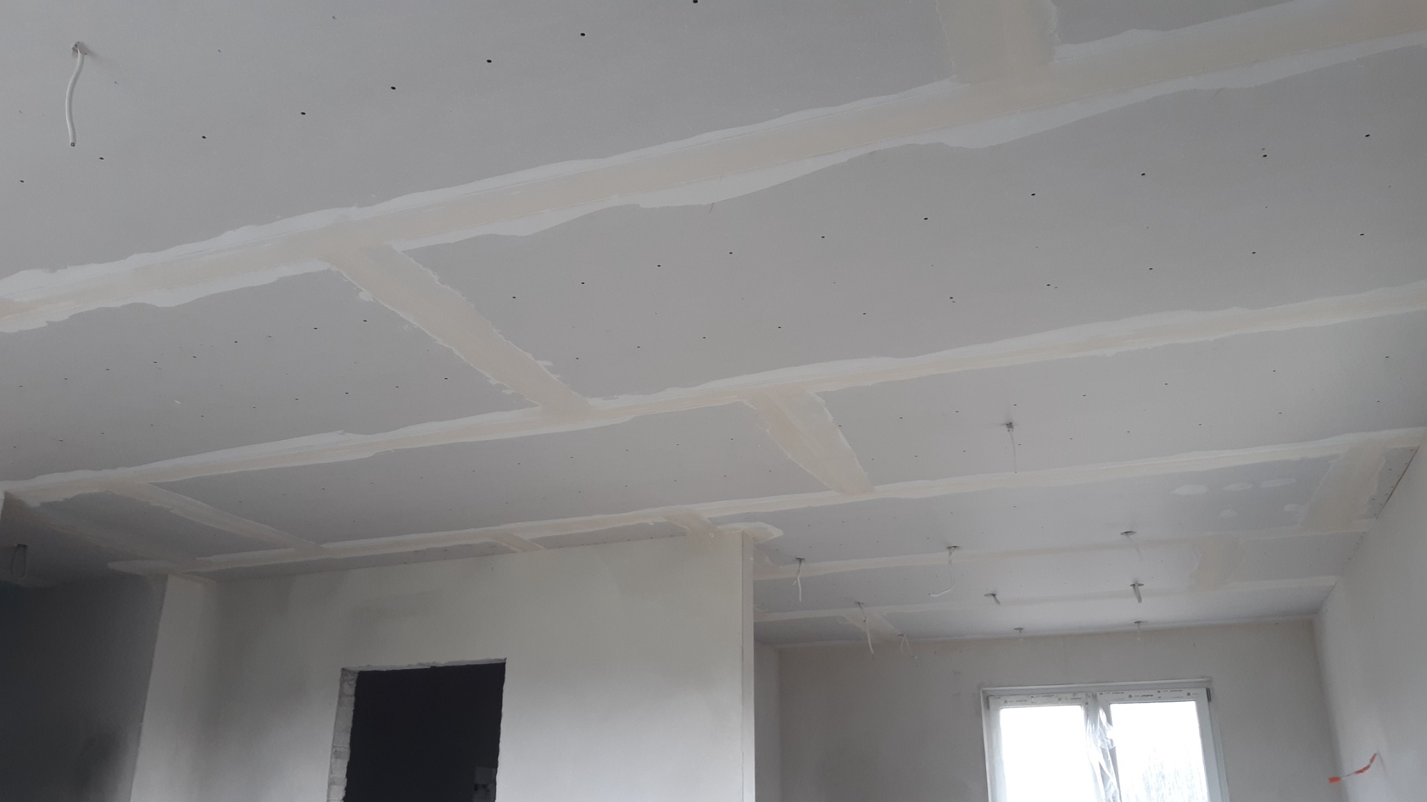 Sufit z płyt gipsowo-kartonowych z widocznymi łączeniami po szpachlowaniu, gotowy do dalszej obróbki, z wystającymi kablami elektrycznymi.