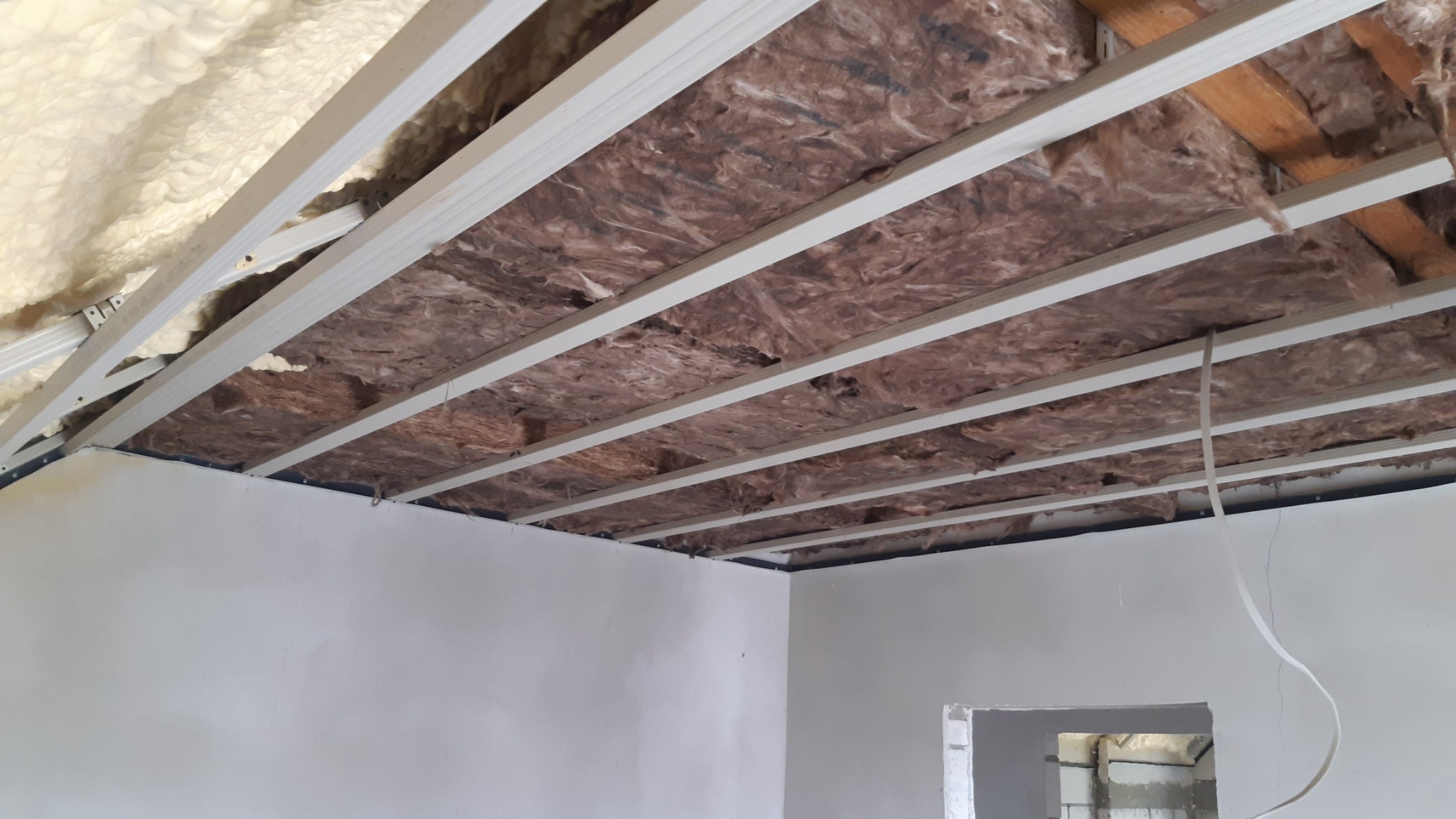Wnętrze w trakcie prac wykończeniowych: ocieplenie poddasza wełną mineralną i pianą, widoczne profile sufitowe oraz fragment ściany przygotowanej do malowania.