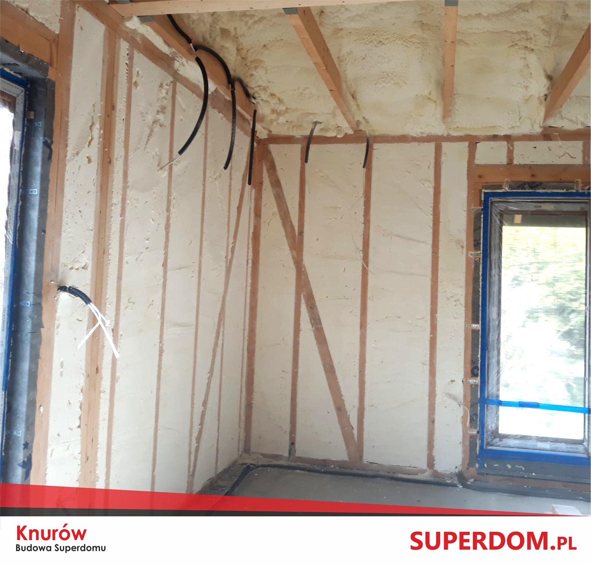 Wnętrze budynku w trakcie budowy: drewniany szkielet konstrukcyjny z ociepleniem pianą PUR, widoczne instalacje elektryczne i okno w niebieskiej folii ochronnej.