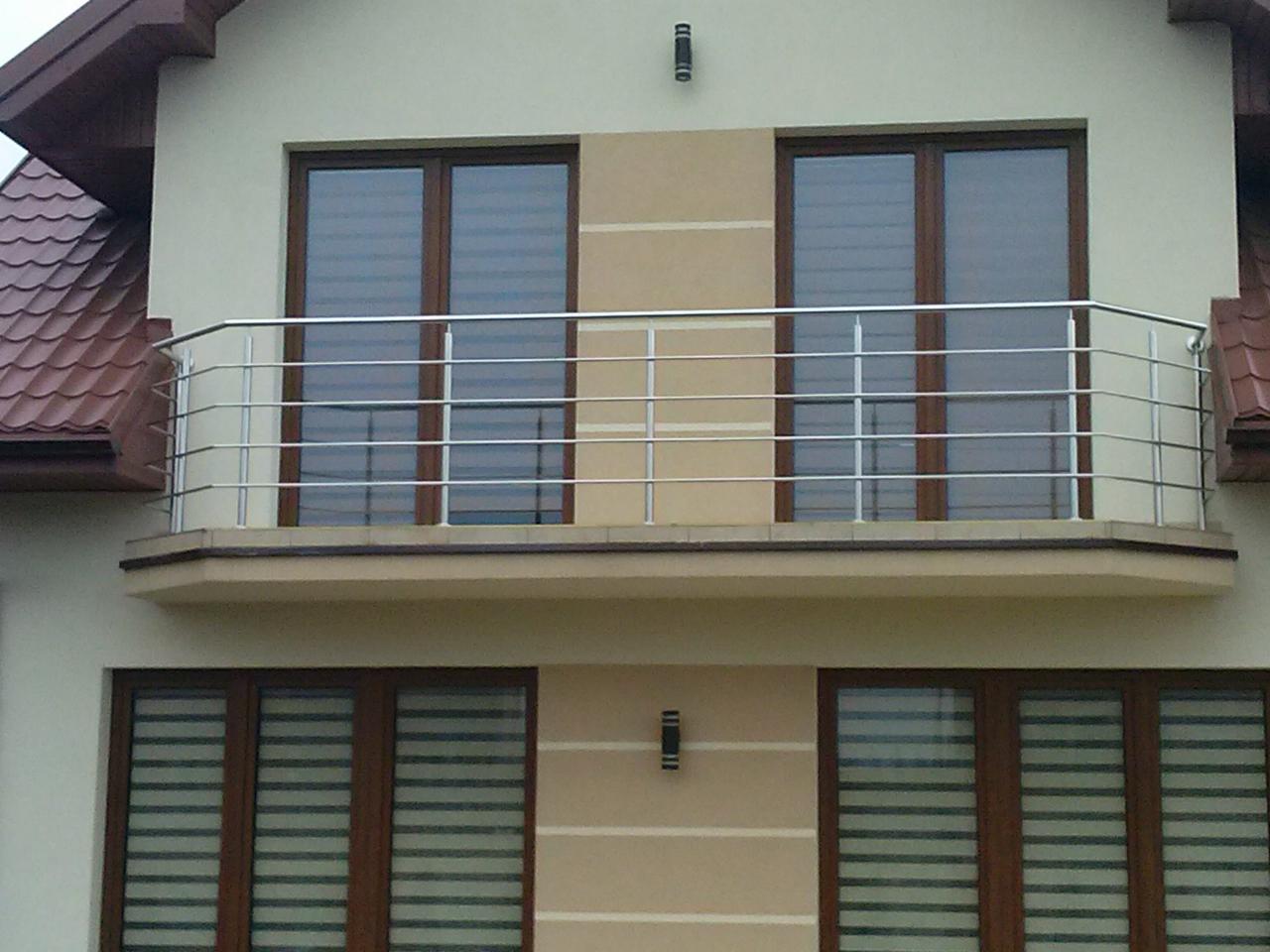 Elegancka, metalowa balustrada balkonowa z poziomymi prętami, zamontowana na balkonie budynku z brązowymi oknami i beżową elewacją. Widok z dołu.