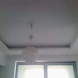 Biały sufit podwieszany z oświetleniem punktowym i wiszącą lampą kulą. Widok z dołu na okno z roletami. Minimalistyczny design wnętrza.