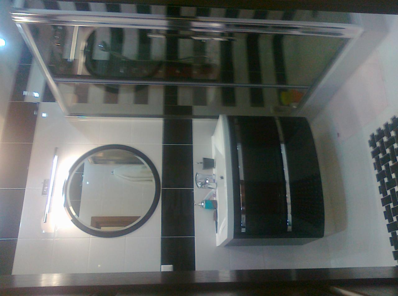 Wykończona łazienka w czarno-białej kolorystyce z okrągłym lustrem i nowoczesną umywalką, widok na kabinę prysznicową z mozaiką na ścianie.