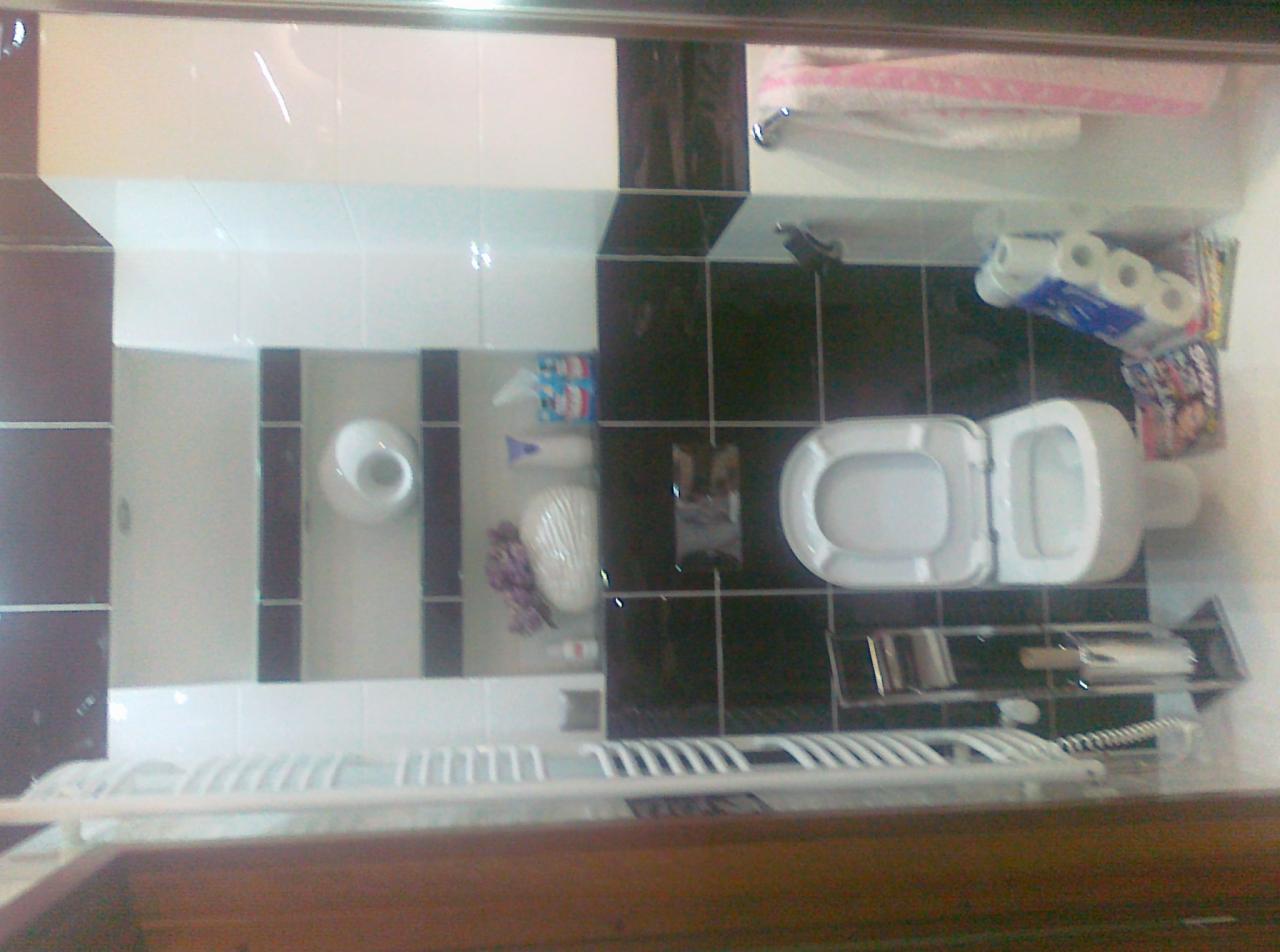 Wykończona łazienka z czarno-białymi płytkami, widok na toaletę, umywalkę i akcesoria łazienkowe. Wyraźne fugi i odbicia w lustrze.