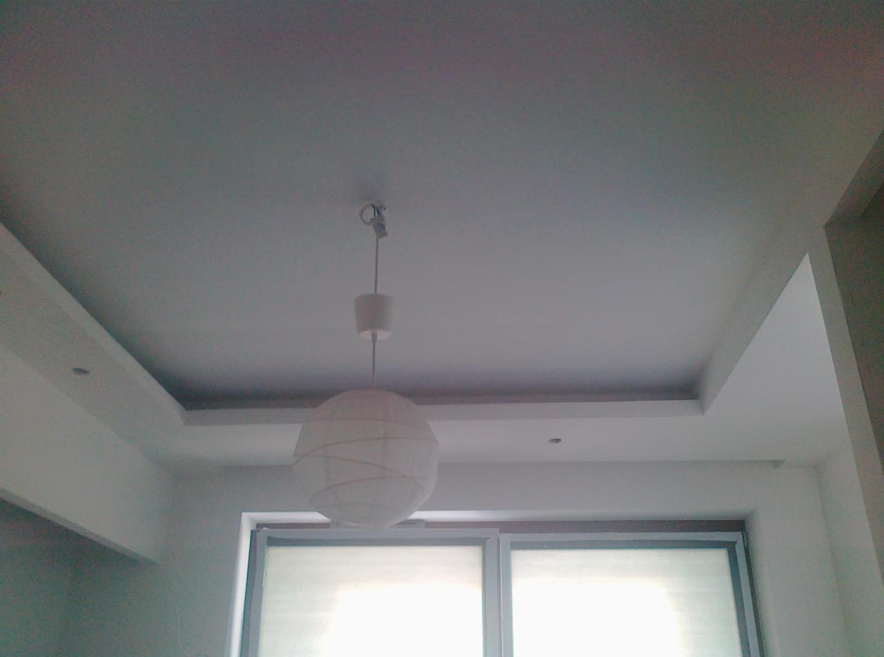 Biały sufit podwieszany z oświetleniem punktowym i wiszącą lampą kulą. Widok z dołu na okno z roletami. Minimalistyczny design wnętrza.