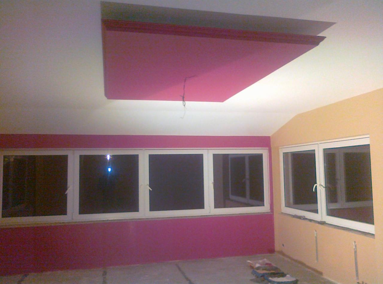 Pokój na poddaszu po malowaniu ścian na różowo i żółto, z oknami i częściowo zamontowanym sufitem podwieszanym w kolorze różowym.