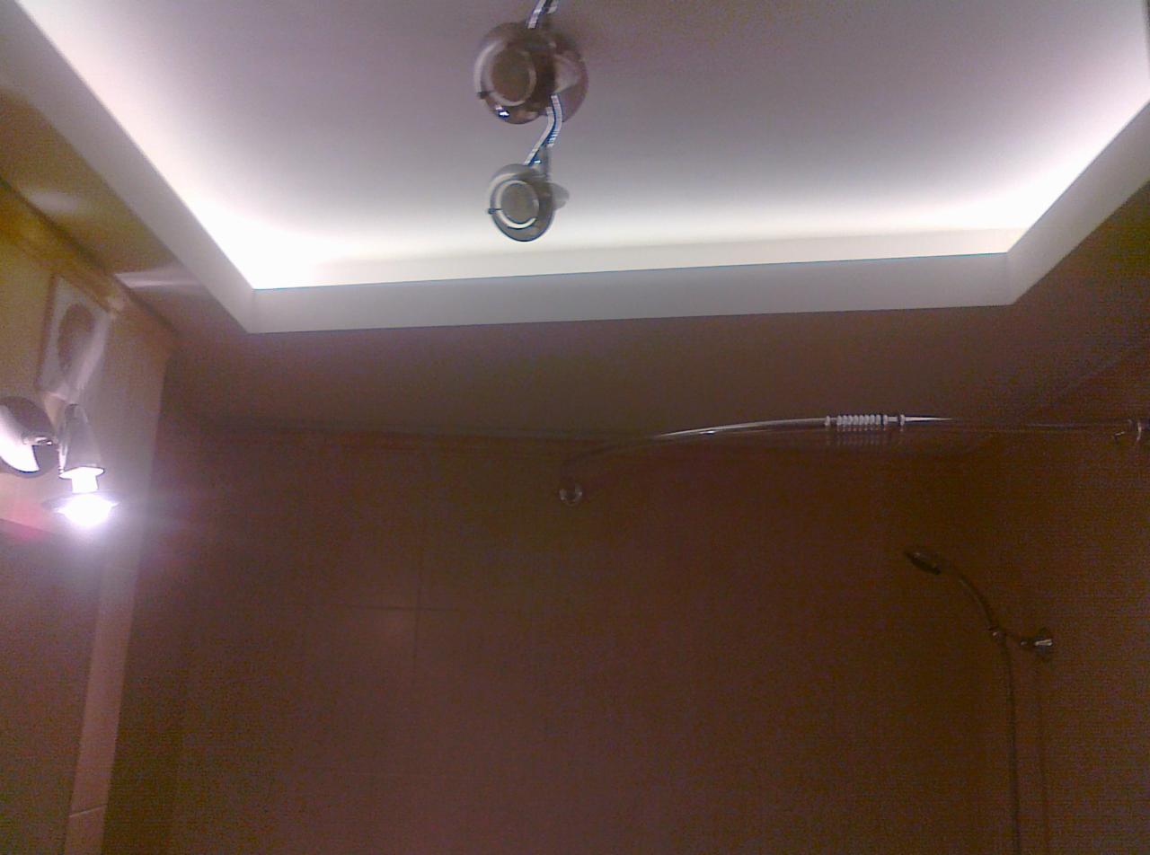 Wykończona łazienka z podwieszanym sufitem z oświetleniem LED. Widoczne płytki na ścianach i elementy instalacji prysznicowej.