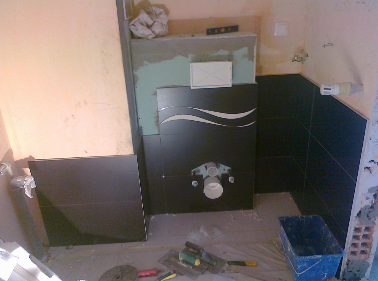 Montaż czarnych płytek z dekoracyjnym wzorem w łazience; widoczna instalacja podtynkowa WC, narzędzia glazurnicze i fragment ściany z płytą gipsową.