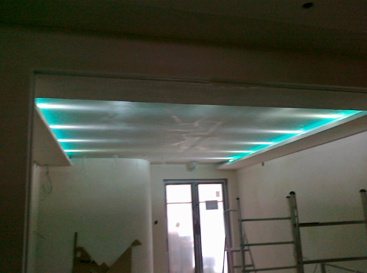 Nowoczesny sufit podwieszany z oświetleniem LED w odcieniach turkusu, widoczny z perspektywy pokoju w trakcie wykańczania, drabina oparta o ścianę.