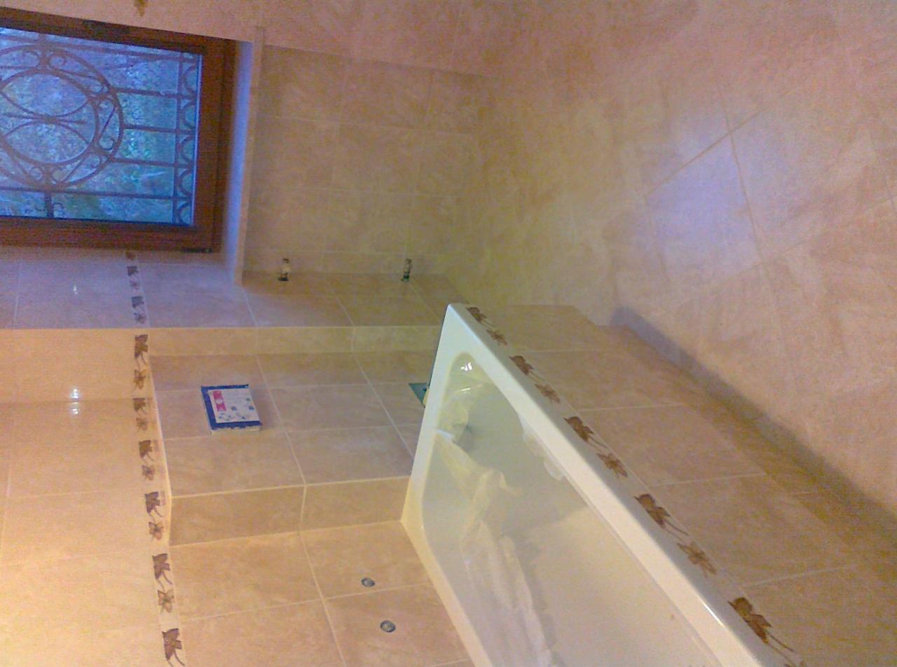 Jasna łazienka po remoncie: beżowe płytki z dekoracyjnym motywem na ścianach i podłodze, widoczna wanna i okno z ozdobną szybą.