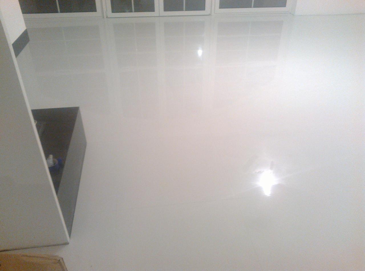 Błyszcząca, biała podłoga z widocznymi refleksami światła i oknami w tle. Minimalistyczne wnętrze, świeżo po wykończeniu. Częściowo widoczna szafka.