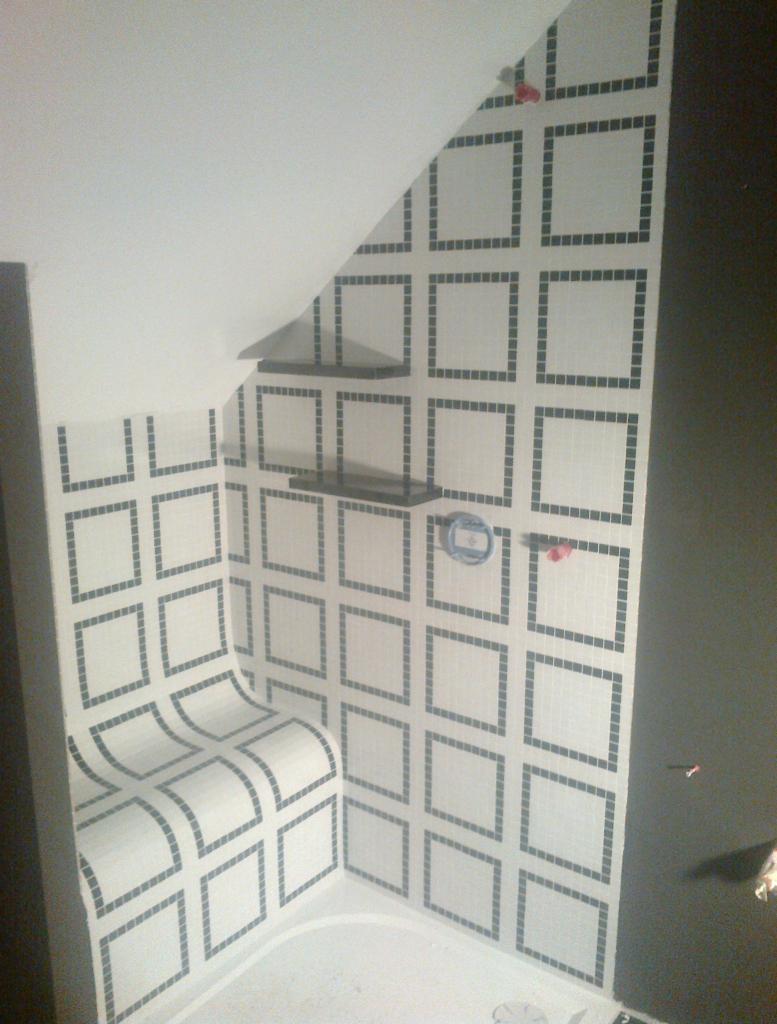 Wykończona kabina prysznicowa z mozaiką w kwadraty, z półkami i siedziskiem. Wzór z białych i szarych płytek. Widok na narożnik kabiny i fragment sufitu.