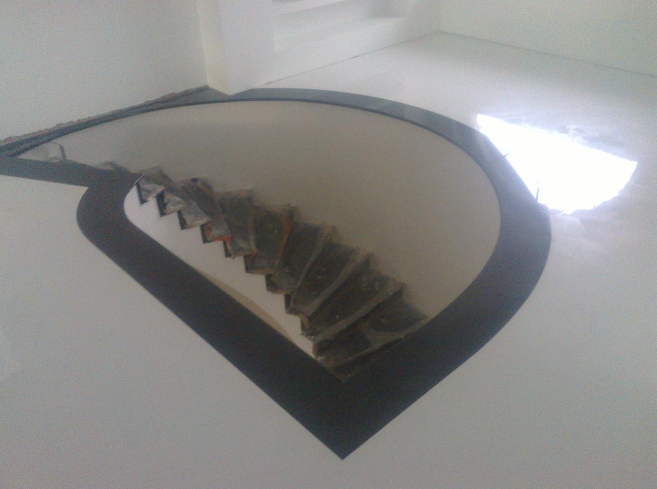 Widok z góry na schody w trakcie wykańczania, zabezpieczone folią, z widocznym obramowaniem w kształcie łuku i prostą, białą podłogą.