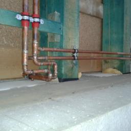 Instalacje-techniczne.pl - Miedziane rury instalacji grzewczej zamocowane do drewnianej konstrukcji w surowym wnętrzu. Widoczne spawy i izolacja z pianki.