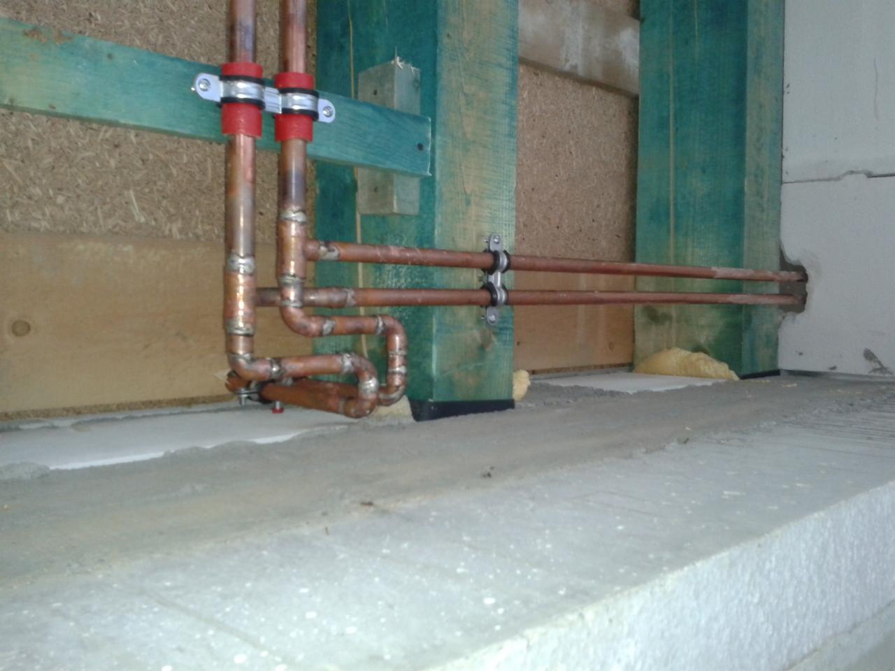 Miedziane rury instalacji grzewczej zamocowane do drewnianej konstrukcji w surowym wnętrzu. Widoczne spawy i izolacja z pianki.