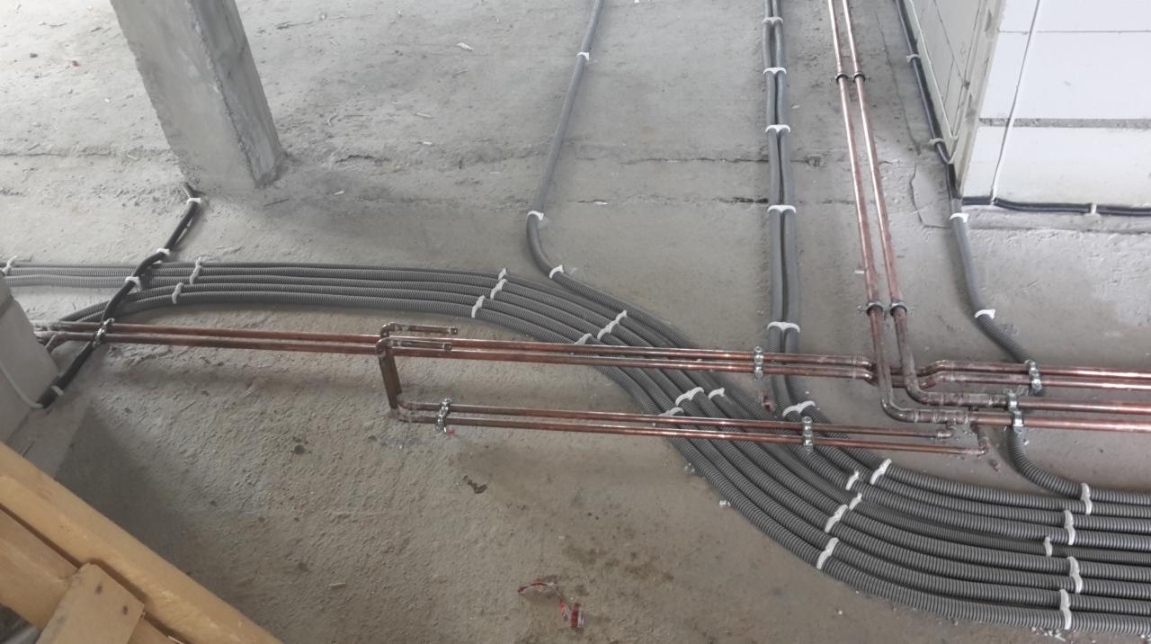 Szczegółowe ułożenie rur miedzianych i peszli instalacji elektrycznej na surowym podłożu wewnątrz budynku, widoczne elementy mocujące.