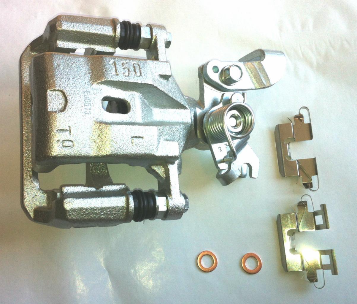 Szary, metalowy zacisk hamulcowy z akcesoriami: sprężyna, blaszki i miedziane podkładki, leżący na jasnym tle. Widoczne ślady obróbki.