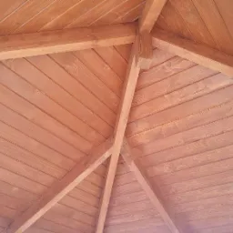 Drewniana konstrukcja dachu altany z desek, widok od dołu, w ciepłym oświetleniu. Realizacja z Jaworzna.