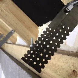 Metalowe łączniki perforowane mocujące drewniane elementy konstrukcji dachu, widoczna piana montażowa i bloczki z betonu komórkowego.