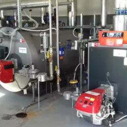 Wnętrze kotłowni z dwoma kotłami grzewczymi Viessmann, widoczne rury, zawory i osprzęt, ślady wycieku na posadzce.