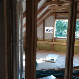 Montaż rekuperacji na poddaszu: widoczne rury wentylacyjne, aluminiowy przewód oraz drewniana konstrukcja dachu z oknami dachowymi.