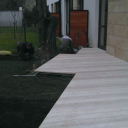 ANKER-GROUP Piotr KOTWICA - Układanie trawy z rolki obok drewnianego tarasu przy nowoczesnym domu, widoczni dwaj pracownicy podczas pracy.