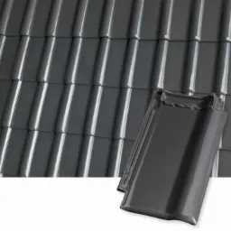 Szare, błyszczące pokrycie dachowe z dachówki ceramicznej, jedna dachówka ułożona na boku na pierwszym planie.