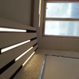 Nowoczesna ściana z podświetleniem LED wzdłuż krawędzi, widok pod kątem. Okno zabezpieczone folią malarską w tle. Wykończenie podłogi w trakcie prac.