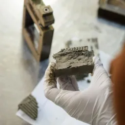 Próbka gruntu w dłoni w białej rękawiczce, obok urządzenie do badania gruntu, widoczne ślady ziemi na rękawiczce.