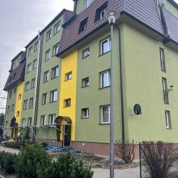 TDL GROUP SP.J. - Wielopiętrowy budynek po malowaniu elewacji, z fragmentami w kolorze żółtym i zielonym. Widoczne rusztowania i pracownicy podczas wykonywania prac malarskich.