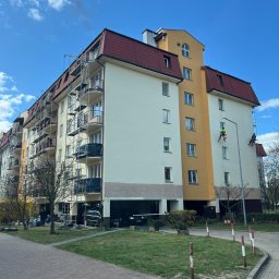 TDL GROUP SP.J. - Wielopiętrowy budynek z rusztowaniami i pracownikami na linach podczas malowania elewacji. Widoczne fragmenty pomalowanej ściany i przygotowane podłoże.