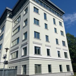 TDL GROUP SP.J. - Odnowiona elewacja budynku biurowego w jasnych barwach, z widocznymi detalami architektonicznymi i świeżo pomalowanymi oknami. Na dole widoczne farby i numeracja.