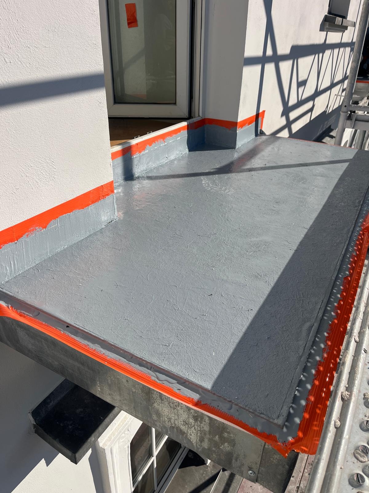 Szary, świeżo zaizolowany balkon z pomarańczową taśmą zabezpieczającą, widok z rusztowania. Nowoczesne wykończenie, detale izolacyjne.