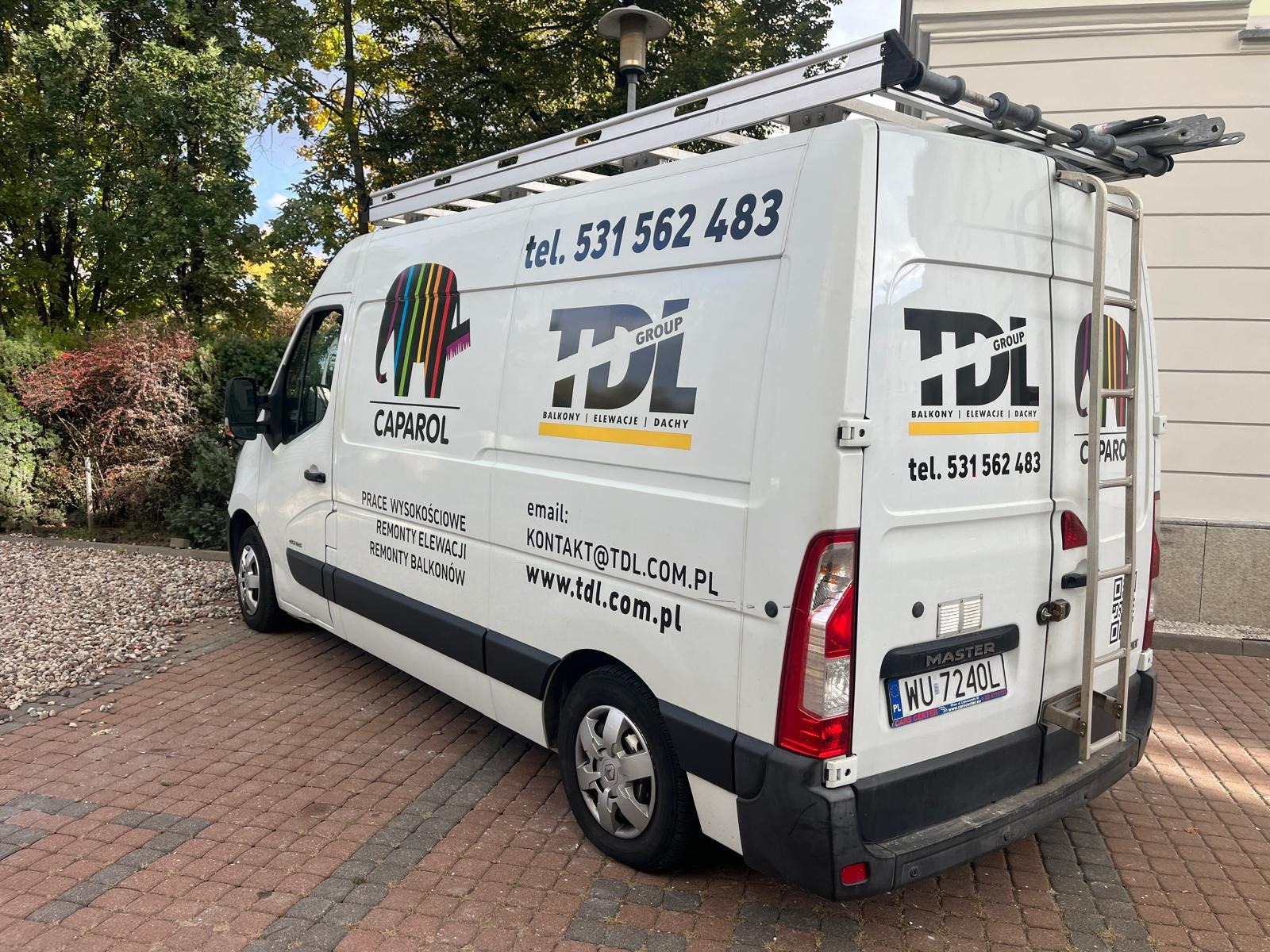 Biały van firmy TDL Group z numerem telefonu, logo i informacjami o usługach: balkony, elewacje, dachy, prace wysokościowe, remonty elewacji i balkonów. Na dachu drabina.