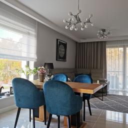 Fom-artdeconstruire-Adam Blachewicz - Nowoczesna jadalnia z drewnianym stołem, turkusowymi krzesłami, błyszczącą podłogą w odcieniach beżu i oryginalnymi lampami sufitowymi w stylu atomowym.