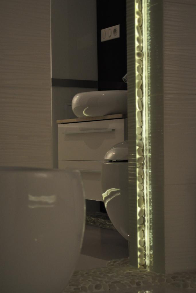 Nowoczesna łazienka z umywalką nablatową, podświetlanym panelem dekoracyjnym i płytkami imitującymi drewno na ścianie, widziana z perspektywy podłogi.