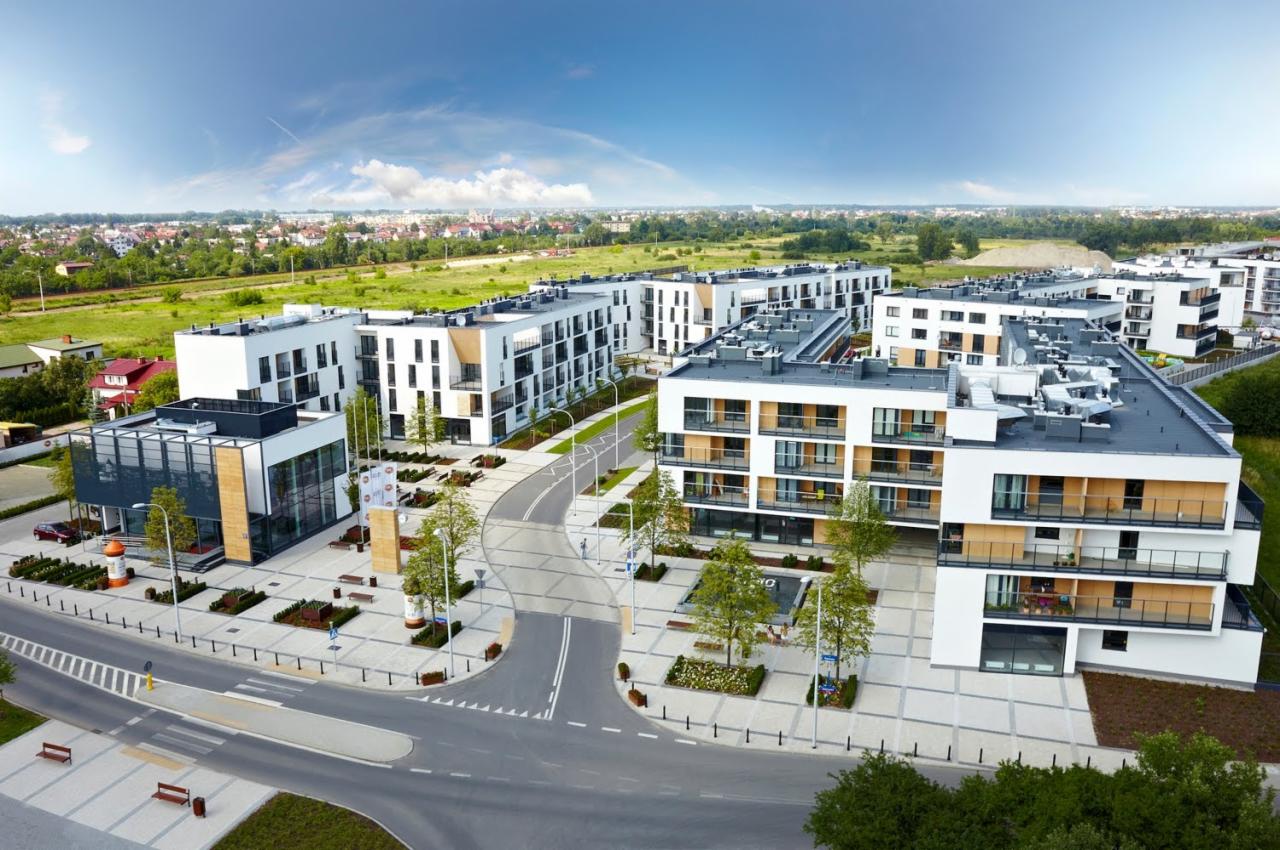 Nowoczesne osiedle budynków wielorodzinnych z zielonymi przestrzeniami, widok z lotu ptaka, błękitne niebo. Charakterystyczna architektura.