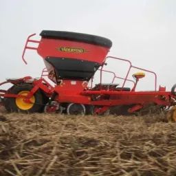 Czerwony siewnik marki Vaderstad w trakcie pracy na polu, widoczne resztki pożniwne i żółte koła maszyny.