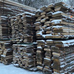Produkcja i handel Artykułami Drzewnymi - Stosy świeżo przetartego drewna, częściowo pokryte śniegiem, z widoczną korą i pomarańczowymi oznaczeniami, składowane na zewnątrz w zimowy dzień.