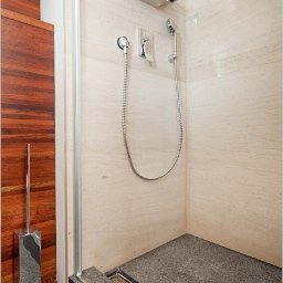 Gnass-Projekty i Realizacje Wnętrz - Nowoczesna kabina prysznicowa z deszczownicą, wykończona jasnym trawertynem i ciemnym, grafitowym kamieniem na podłodze z odpływem liniowym. Drewniane elementy wykończeniowe widoczne obok kabiny.