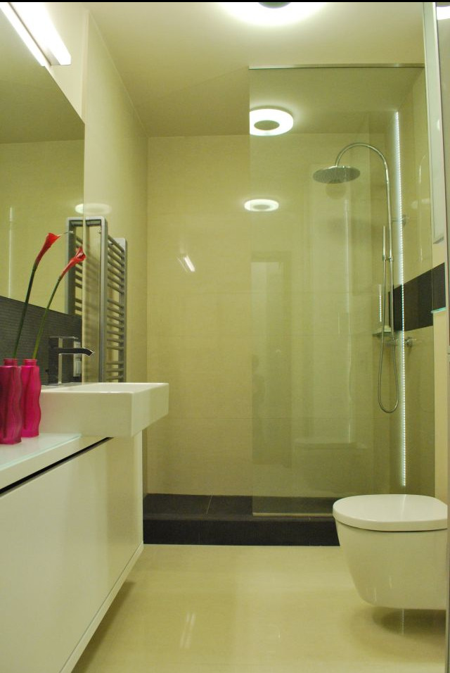 Nowoczesna łazienka z kabiną prysznicową typu walk-in, umywalką nablatową, grzejnikiem drabinkowym i akcentami w postaci różowych kwiatów kalii w wazonie.